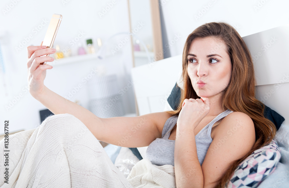 Young girl in bed taking selfie making duck face