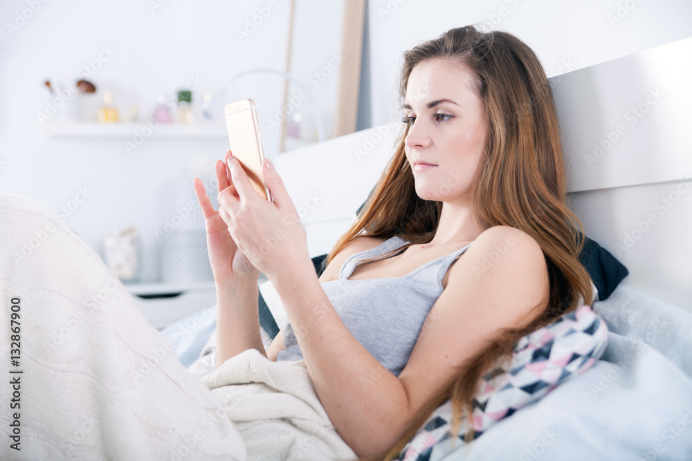 Young woman checking her smartphone lying in bed