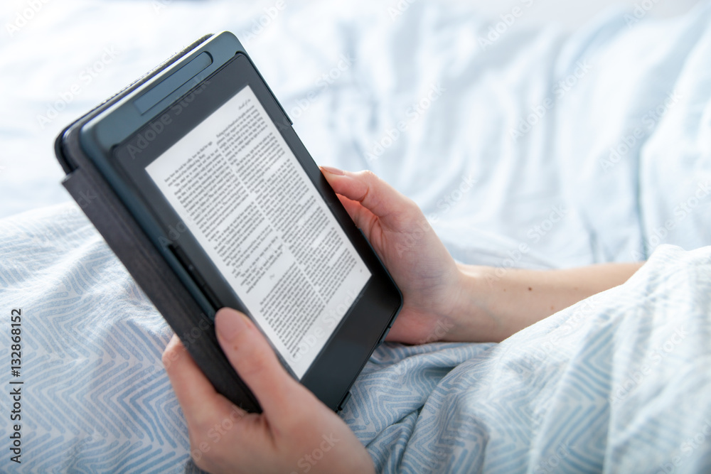 Girl reading ebook on tablet reader in bed at home