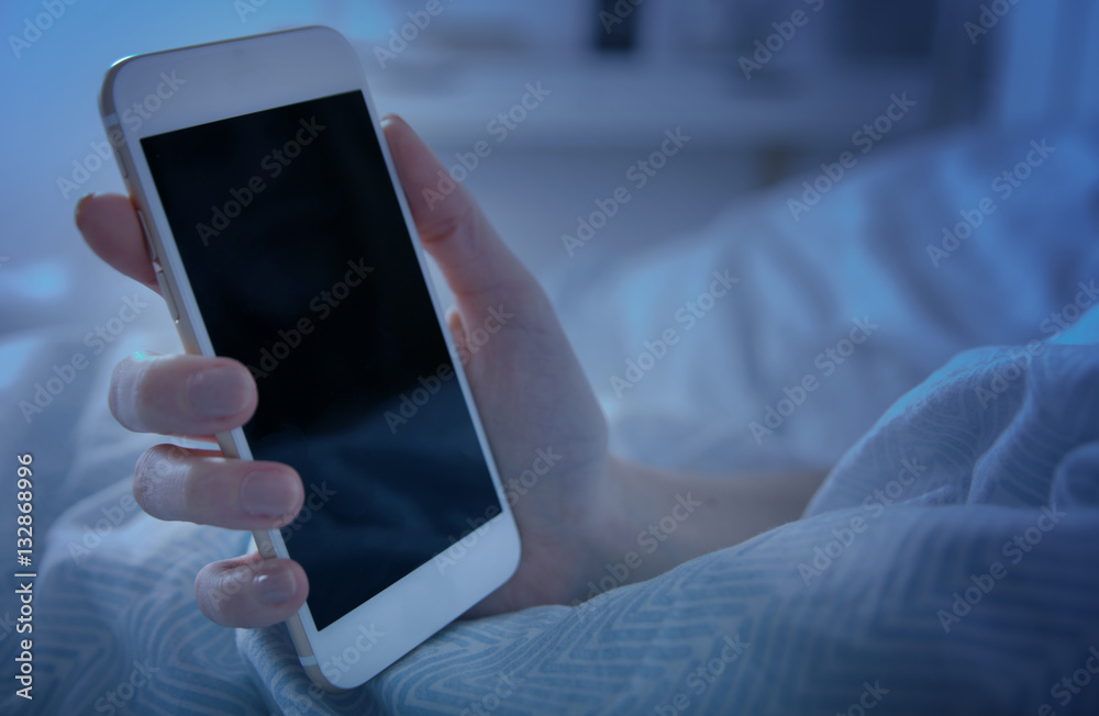 Girl in bed holding smart phone at night close up, blank screen