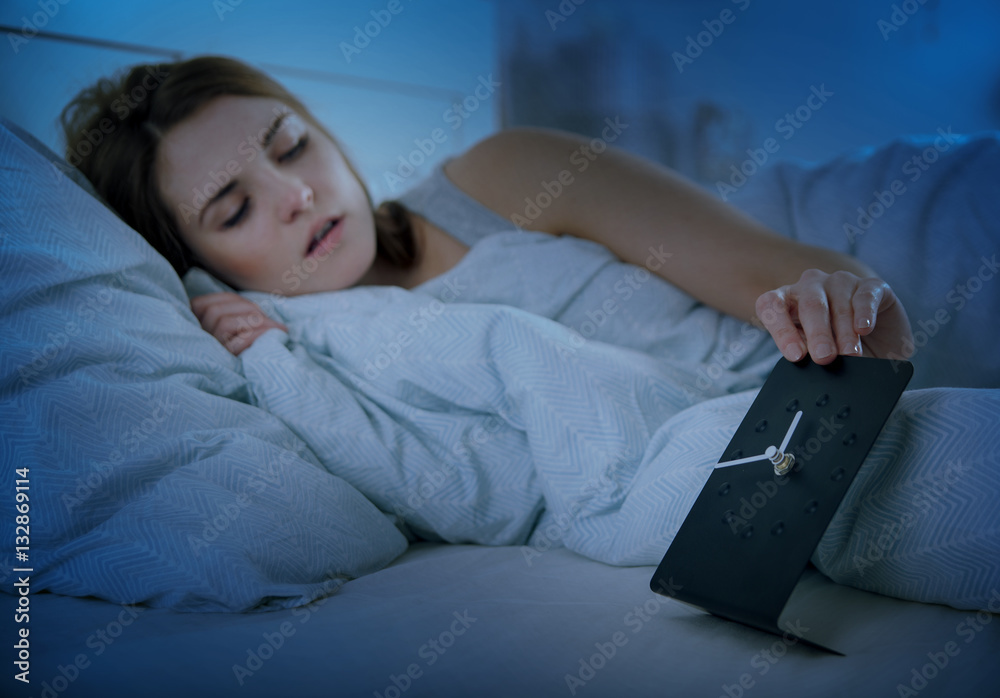 Girl in bed at night checking clock, insomnia sleeping problem concept