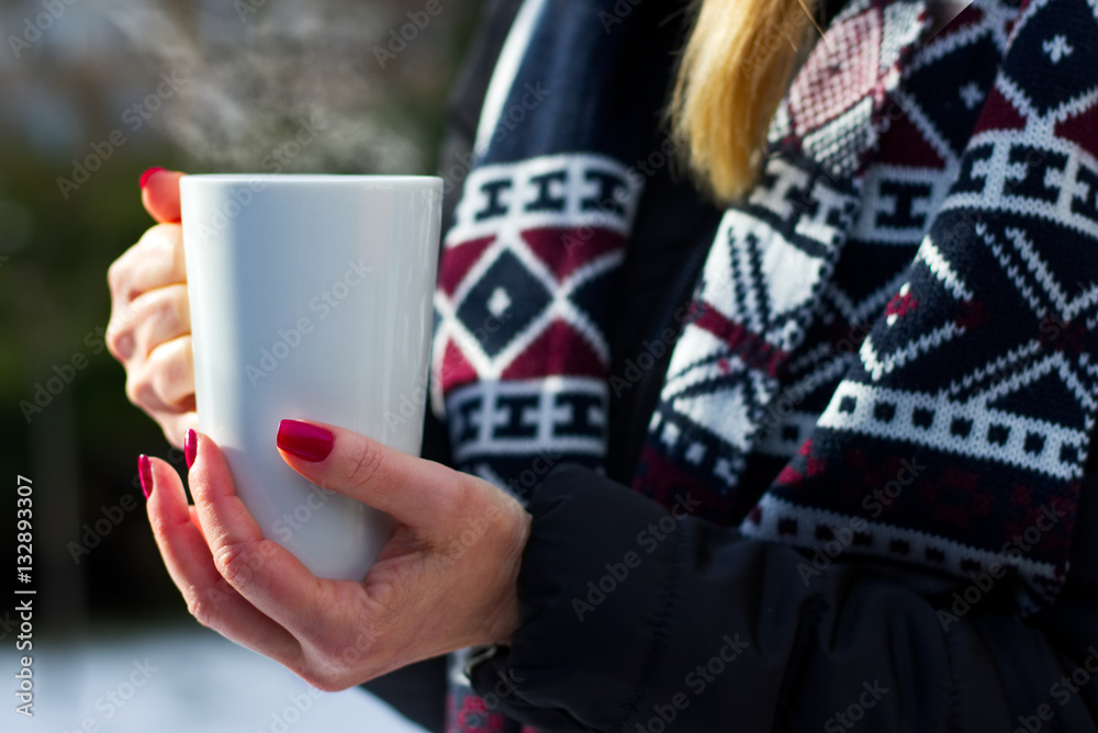 woman holding a steaming hot cup of coffee in her hands outdoors in winter, numbed female hands with