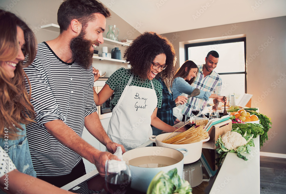 Large group of six friends cooking pasta at table