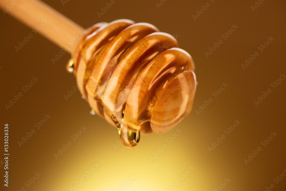 Honey dripping from honey dipper isolated on yellow. Thick honey dipping from the wooden honey spoon