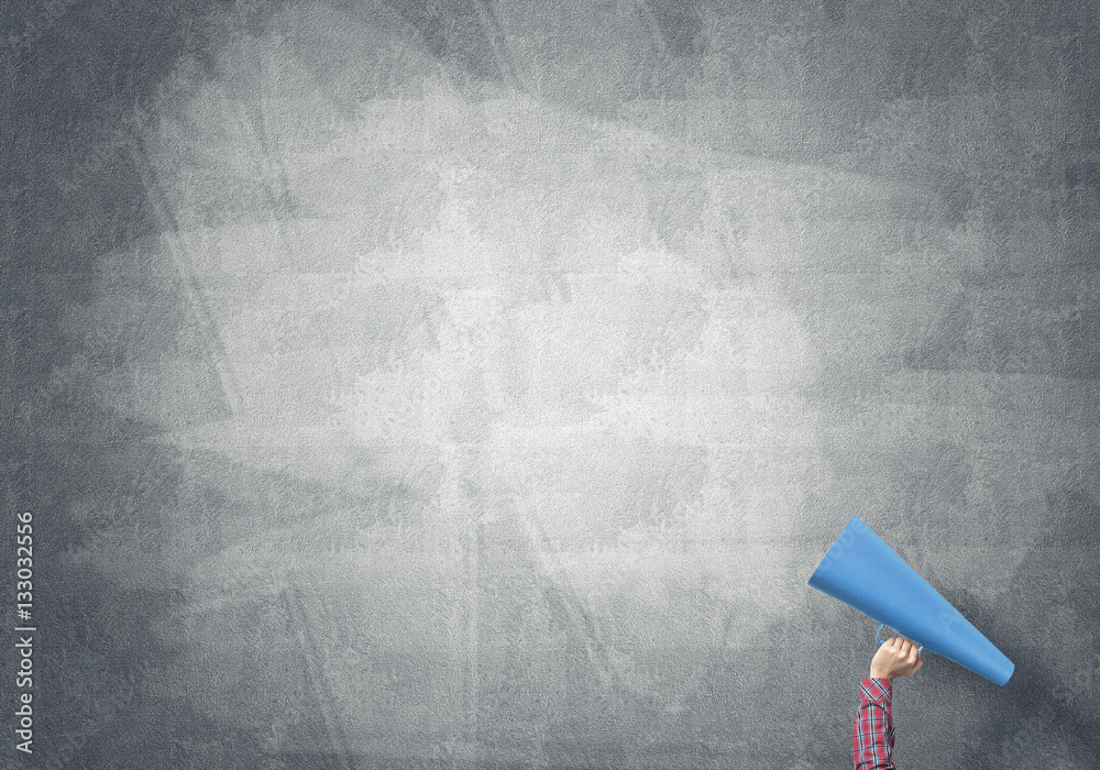 Hand of woman holding paper trumpet against concrete background