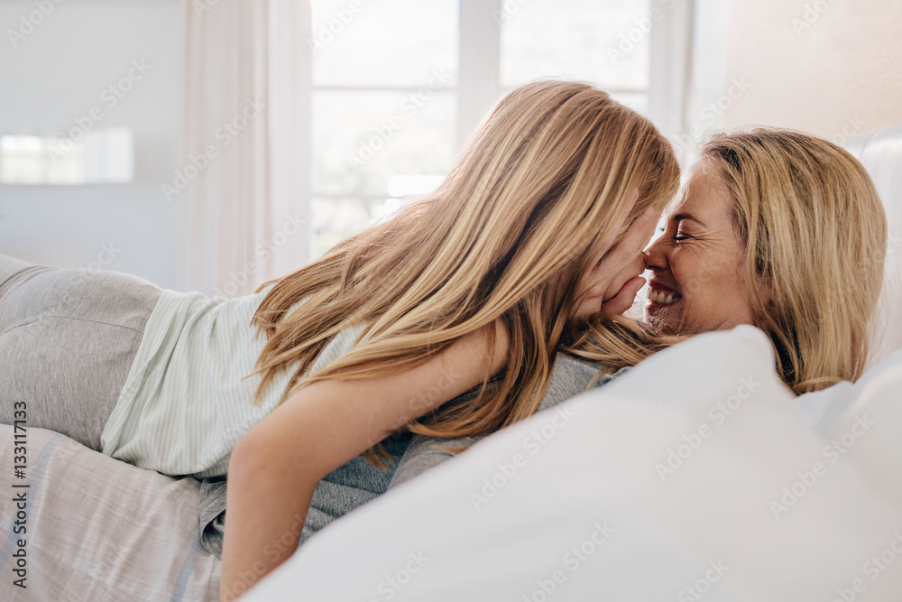 Smiling mother and daughter playing in bedroom