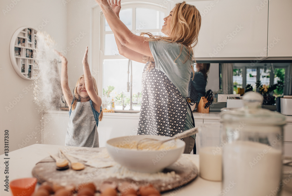 Happy young mother and daughter having fun in kitchen