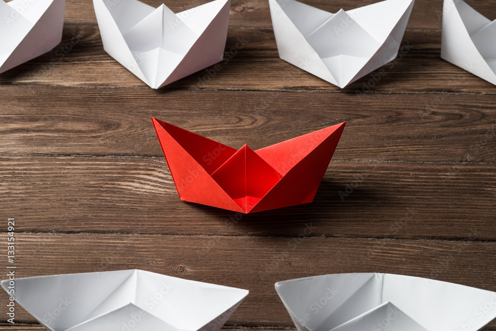 Business leadership concept with white and color paper boats on wooden table