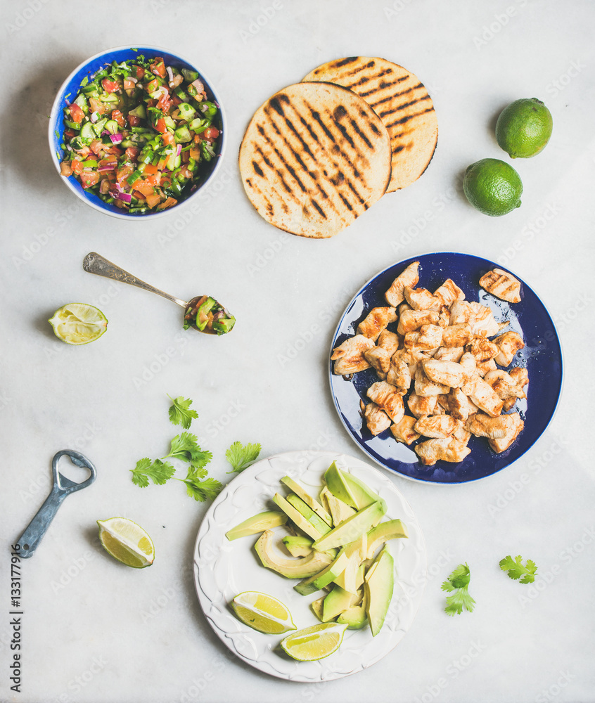 Ingredients for cooking chicken and avocado tacos. Fresh salsa, limes, grilled corn tortillas, grill