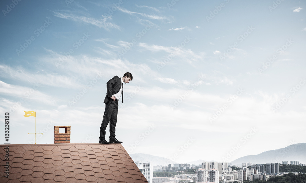 Businessman looking down from roof and afraid to make step. Mixe