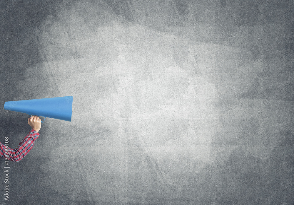 Hand of woman holding paper trumpet against concrete background