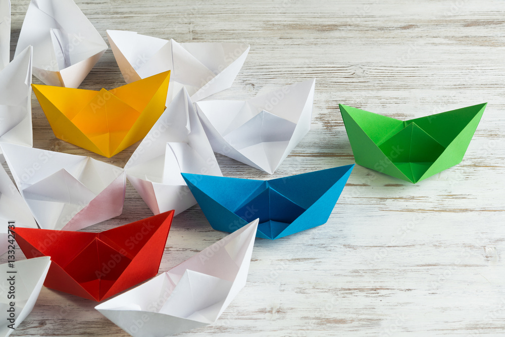 Business leadership concept with white and color paper boats on wooden table