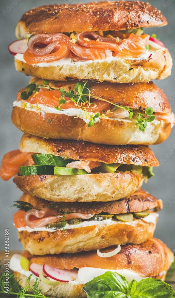 Heap of Bagels with salmon, eggs, vegetables, capers, fresh herbs and cream-cheese, grey concrete ba