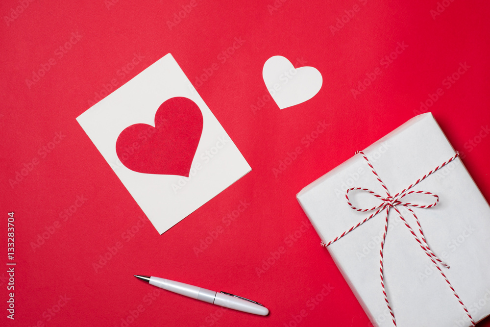 Handmade small gift box with heart symbol on red background.