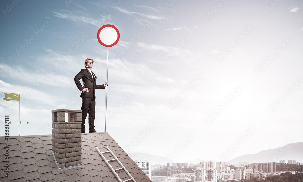 Caucasian businessman on brick house roof showing stop road sign