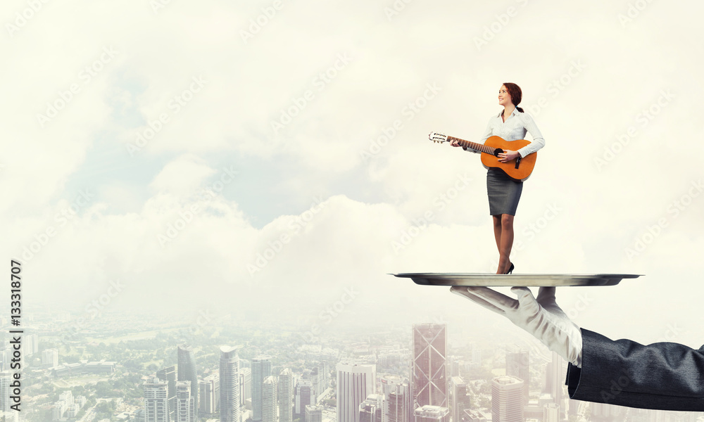 Attractive businesswoman on metal tray playing acoustic guitar against cityscape background