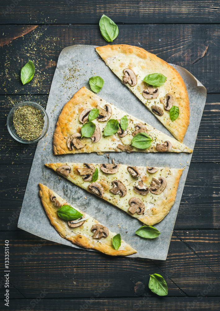 Homemade mushroom pizza with basil cut in slices and spices in glass on baking paper over dark scorc