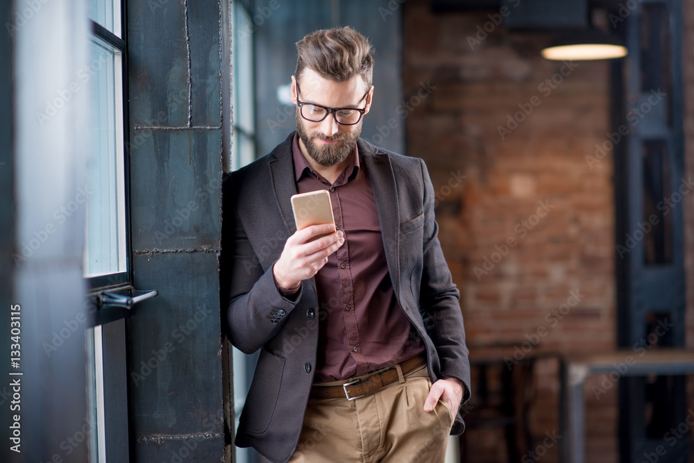 Handsome caucasian businessman dressed in the suit reading with his smart phone near the window in t