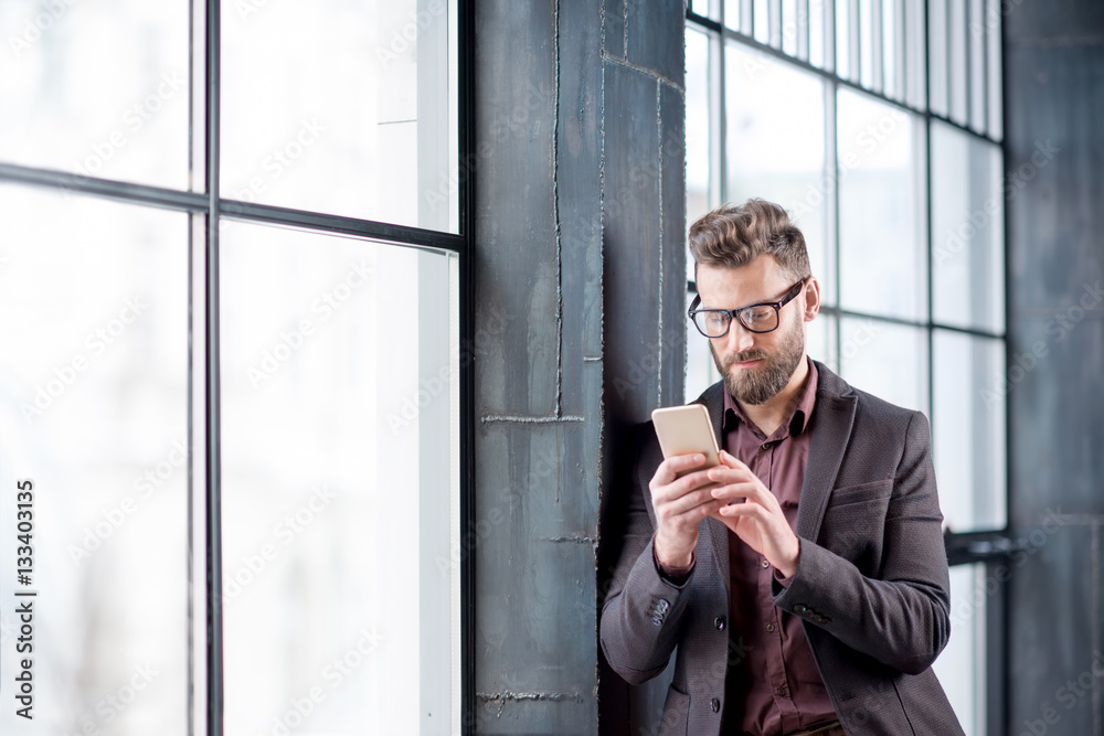 Handsome caucasian businessman dressed in the suit reading with his smart phone near the window in t