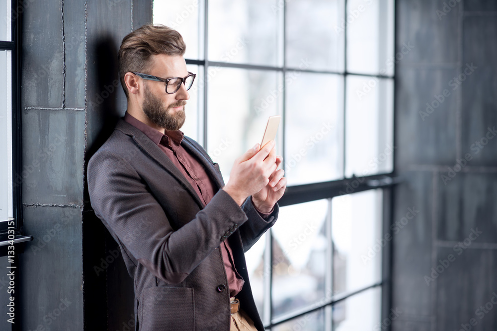 Handsome caucasian businessman dressed in the suit reading with his smart phone near the window in t