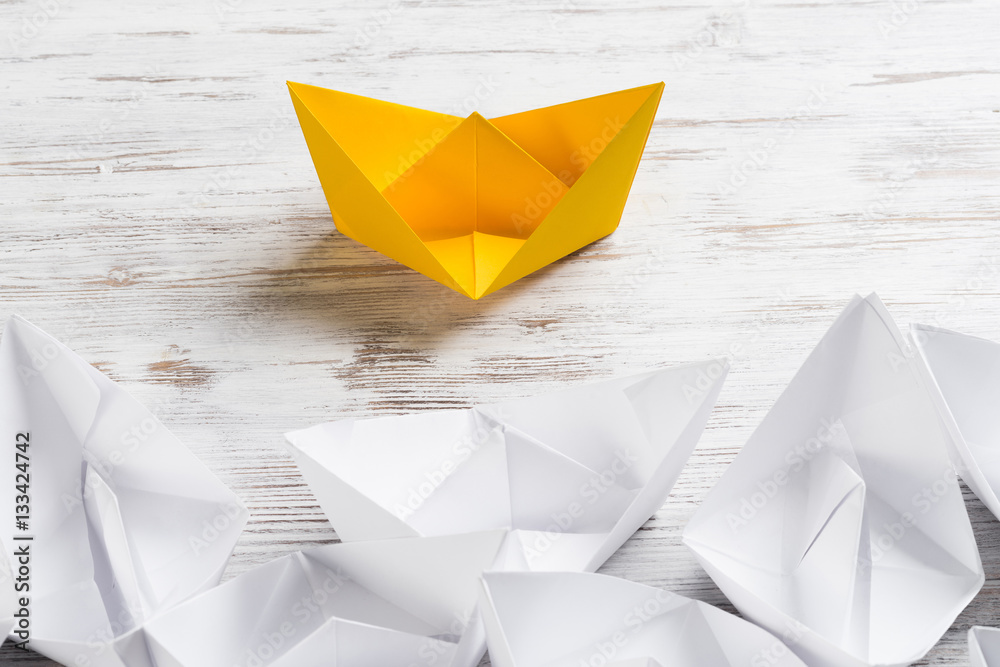 Business leadership concept with white and color paper boats on wooden table