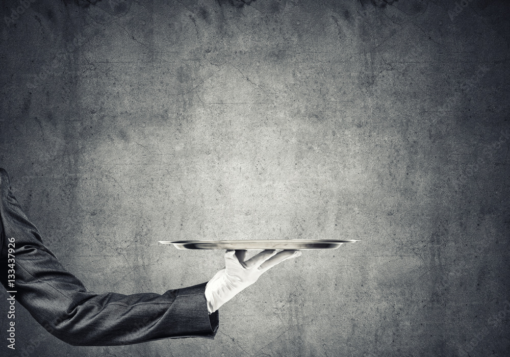 Hand of butler holding empty metal tray against concrete background