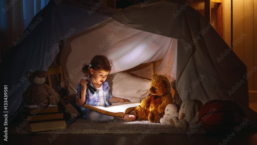 child girl with a book and a flashlight and teddy bear before go