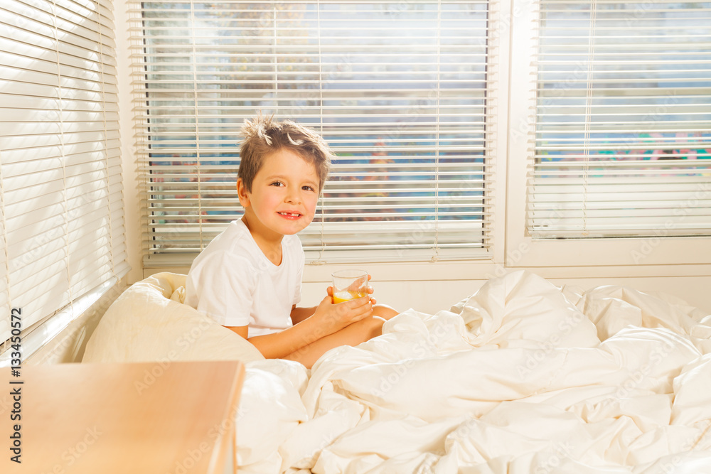 Little boy drinking orange juice sitting in bed