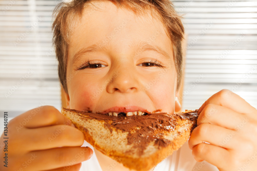 Happy kid boy eating toast with chocolate spread