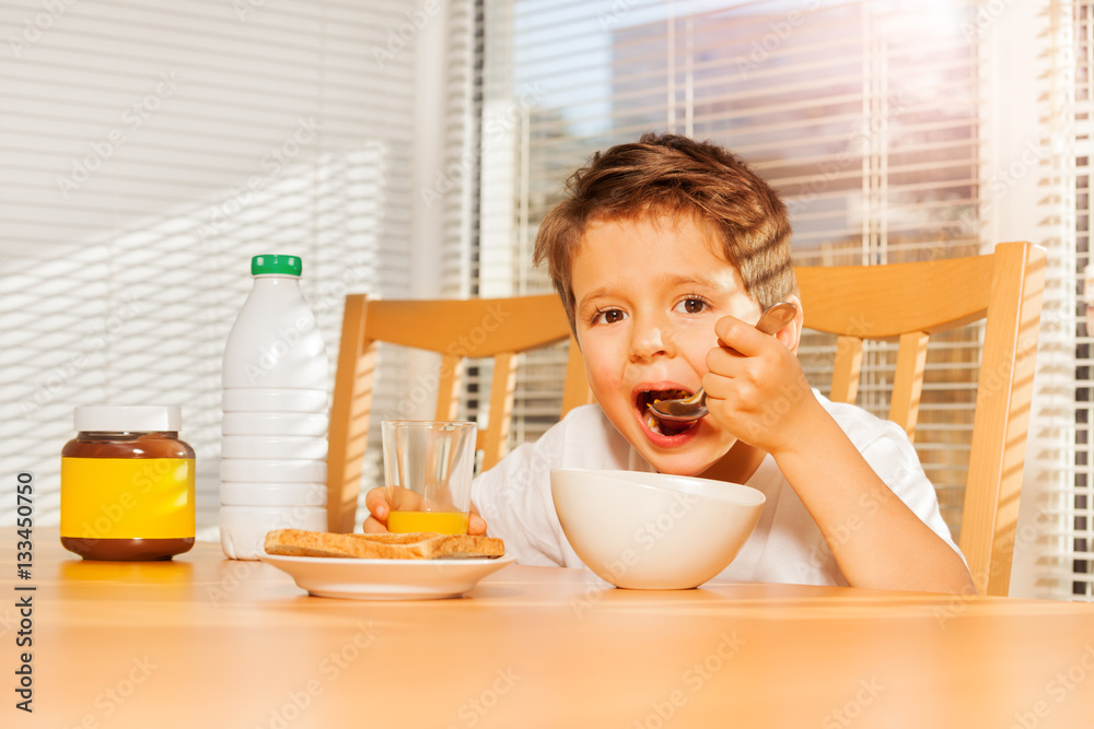 Adorable little boy eating corn flakes in kitchen