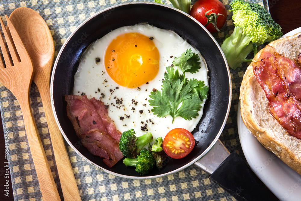 Breakfast with fried egg and bacon in dark pan on the table