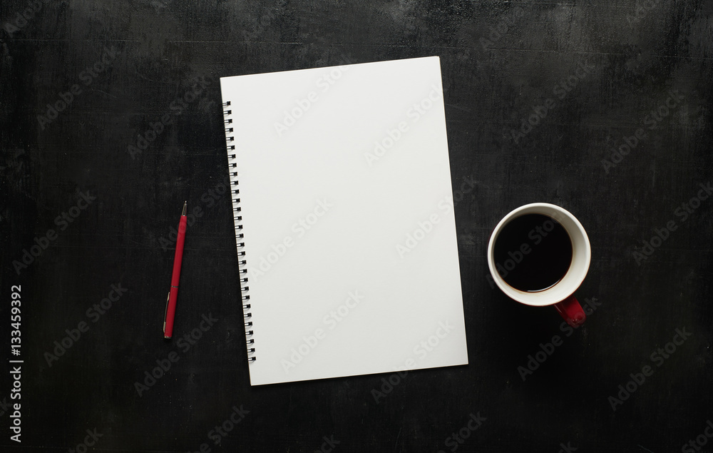 Wooden black office desk table with notebook, pen and  cup of coffee. Blank notebook page for input 