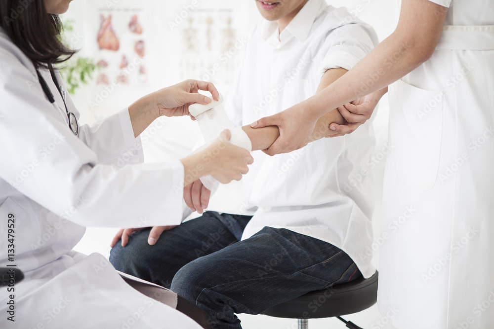 The doctor is wrapping a bandage in the hand of a man