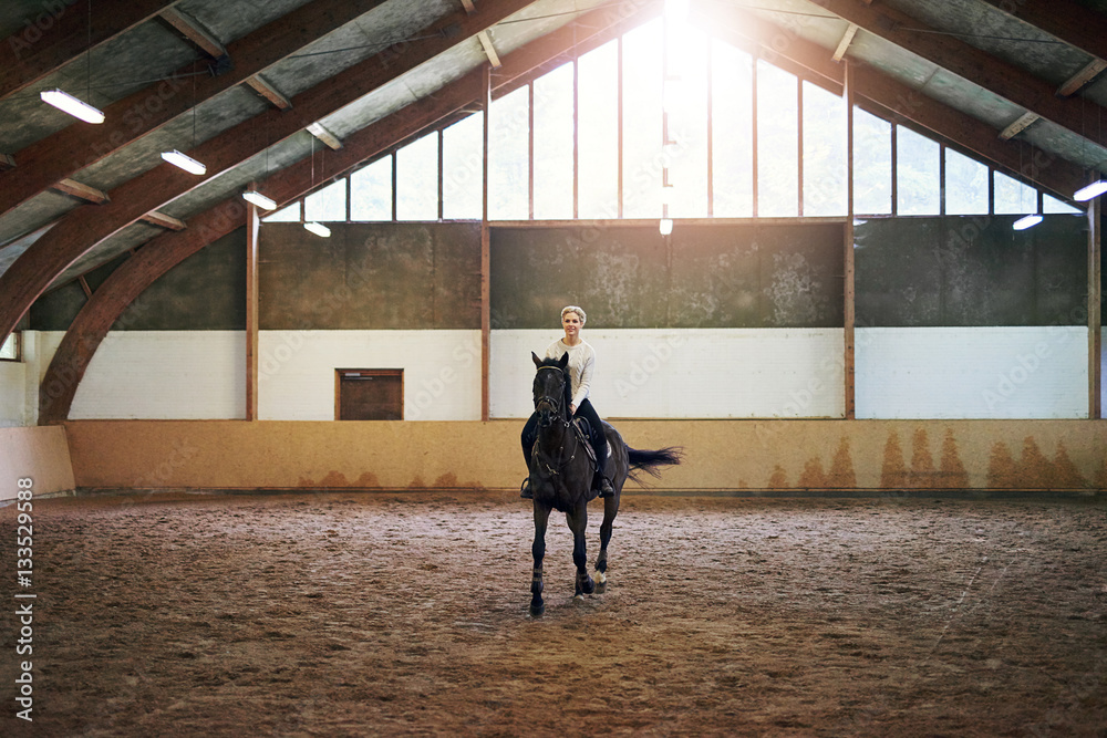 Female riding dark horse in indoor paddock