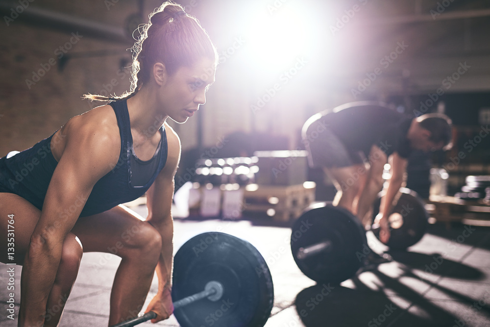 Muscular man and woman lifting heavy barbells