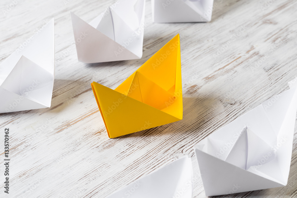 Business leadership concept with white and color paper boats on wooden table