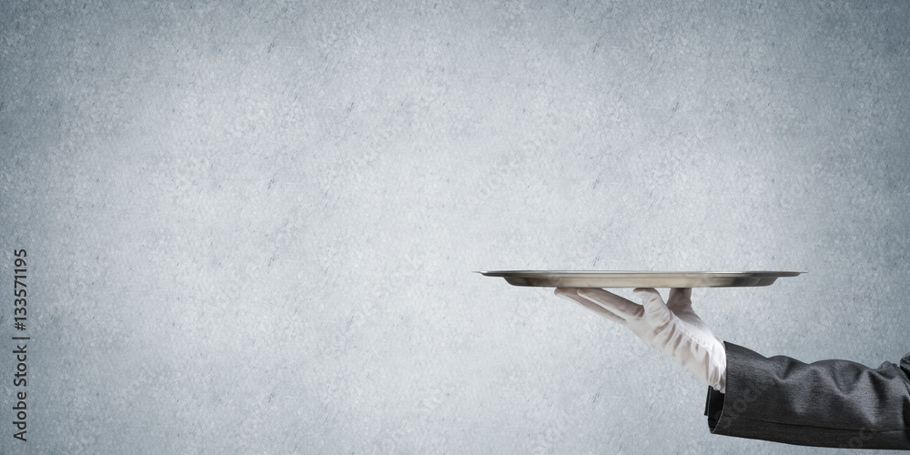 Hand of butler holding empty metal tray against concrete background