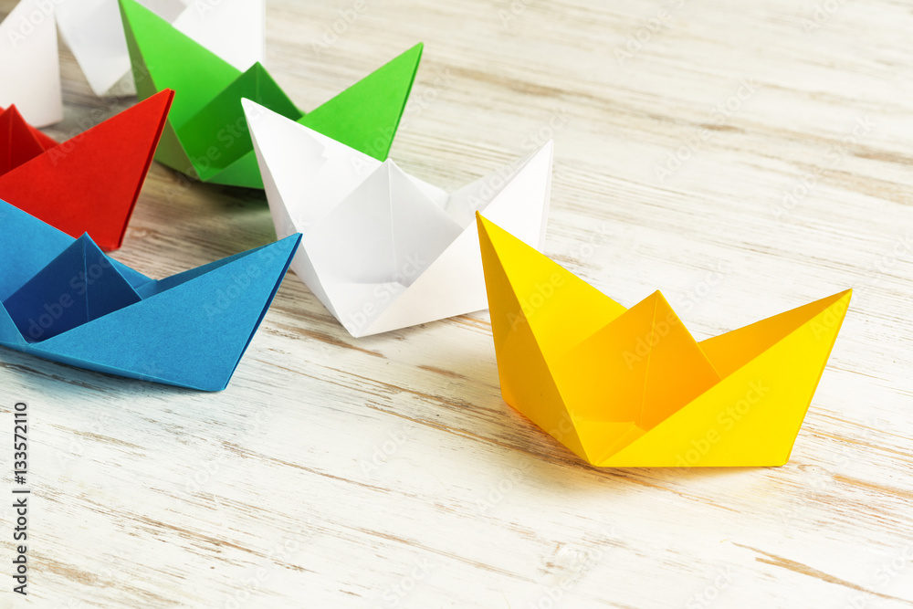 Business leadership concept with white and color paper boats on wooden table