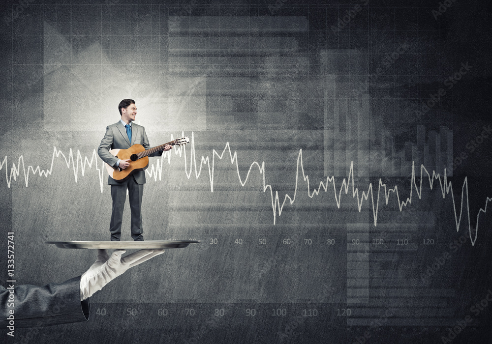 Businessman on metal tray playing acoustic guitar against graphs background