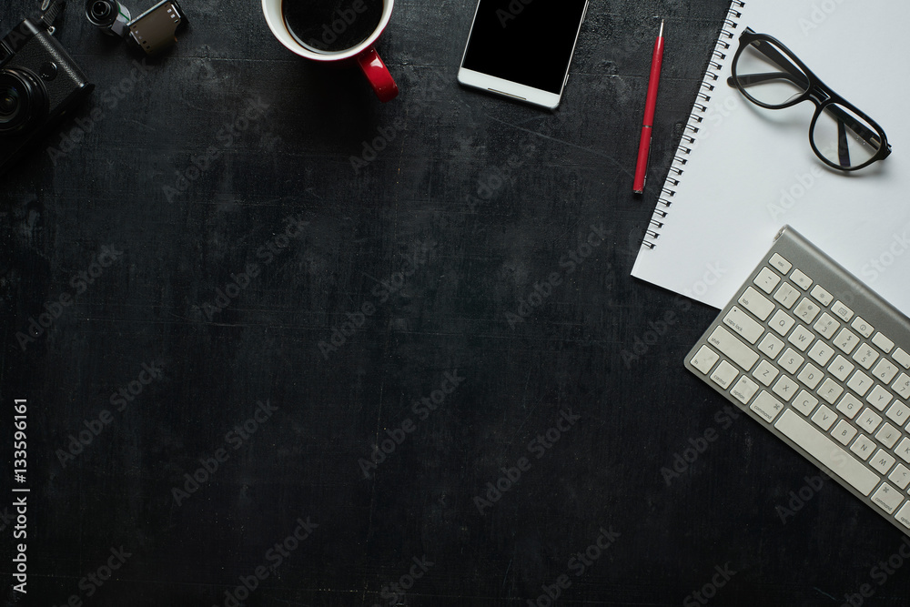 Wooden black office desk table with notebook, camera and other supplies with cup of coffee. Blank no