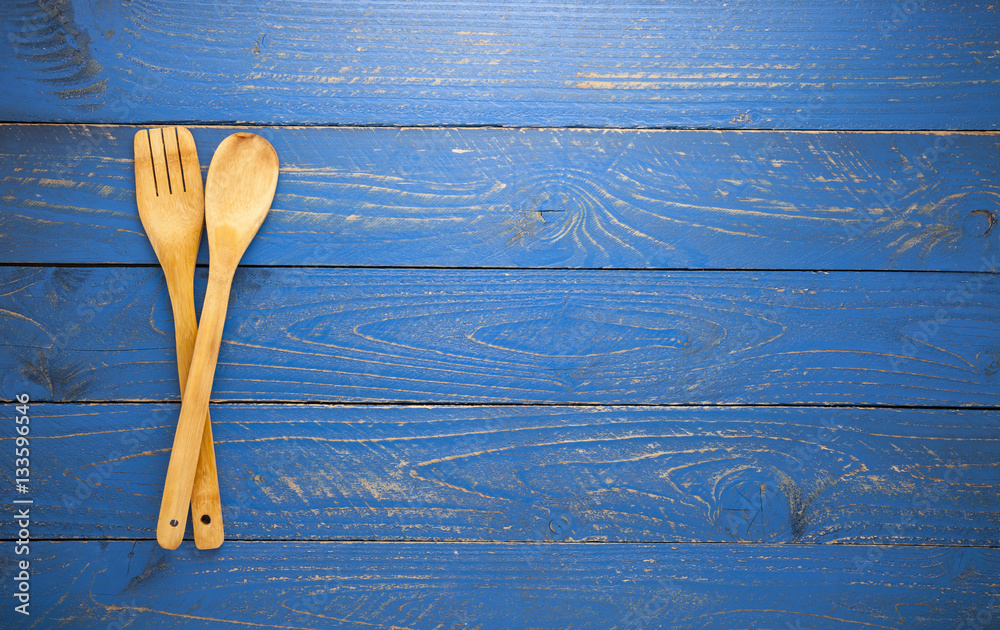 Wooden spoon and fork on blue wood table background.