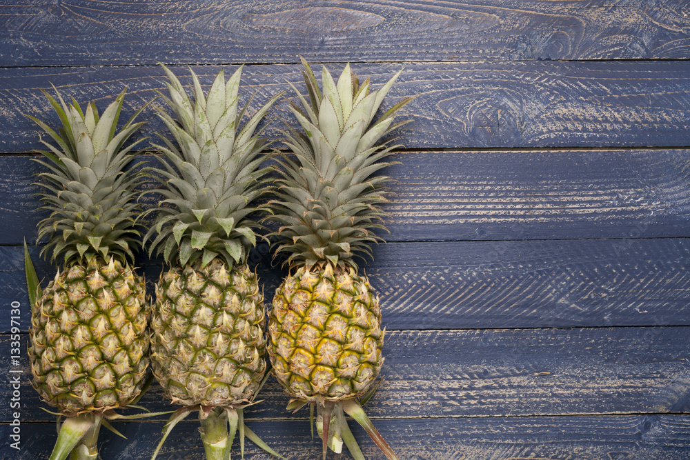  Row of pineapple fruits on wooden table background.