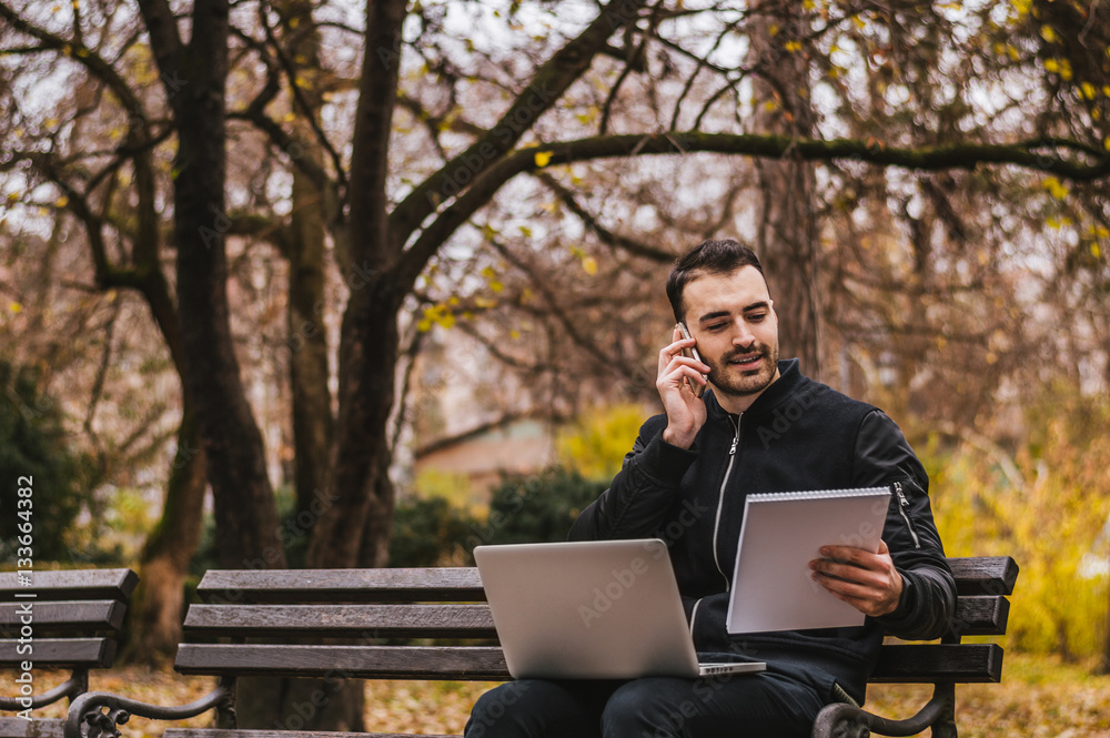 Contemporary young businessman working on his laptop in a park