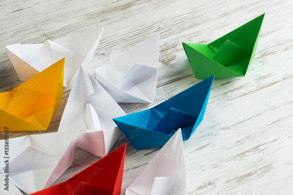 Business leadership concept with white and color paper boats on wooden table