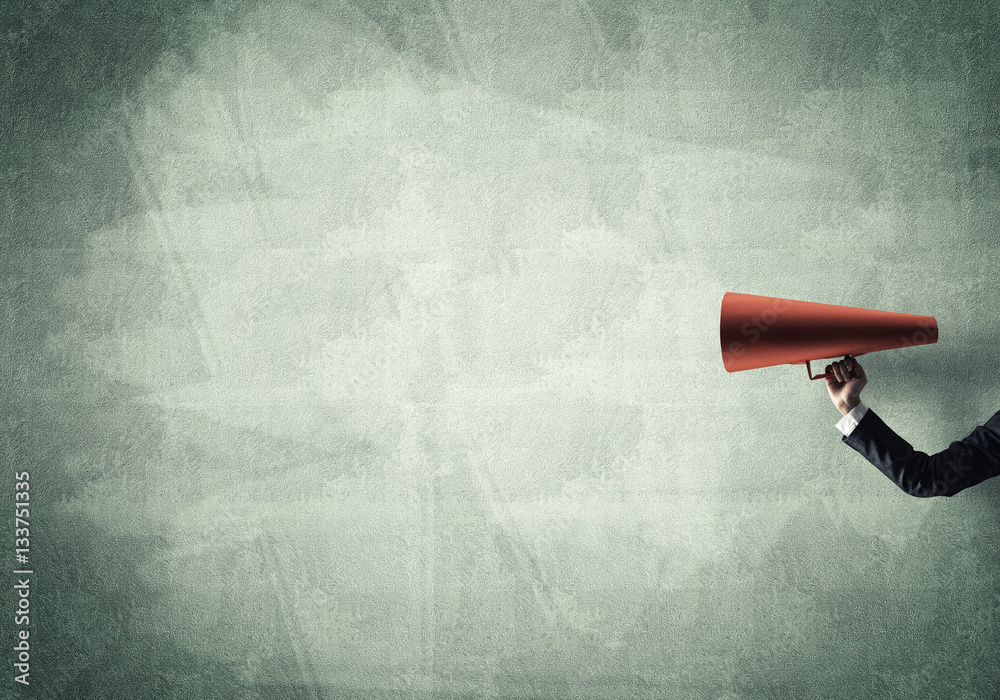 Hand of businesswoman holding red paper trumpet against concrete background