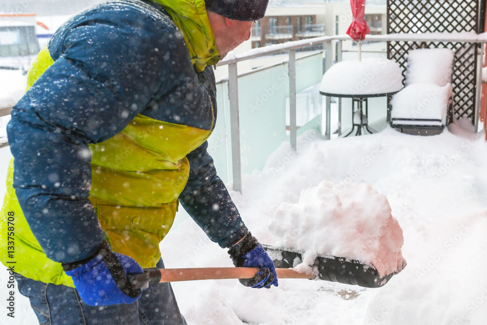 Man shoveling the show on the terrace after heavy snowfall