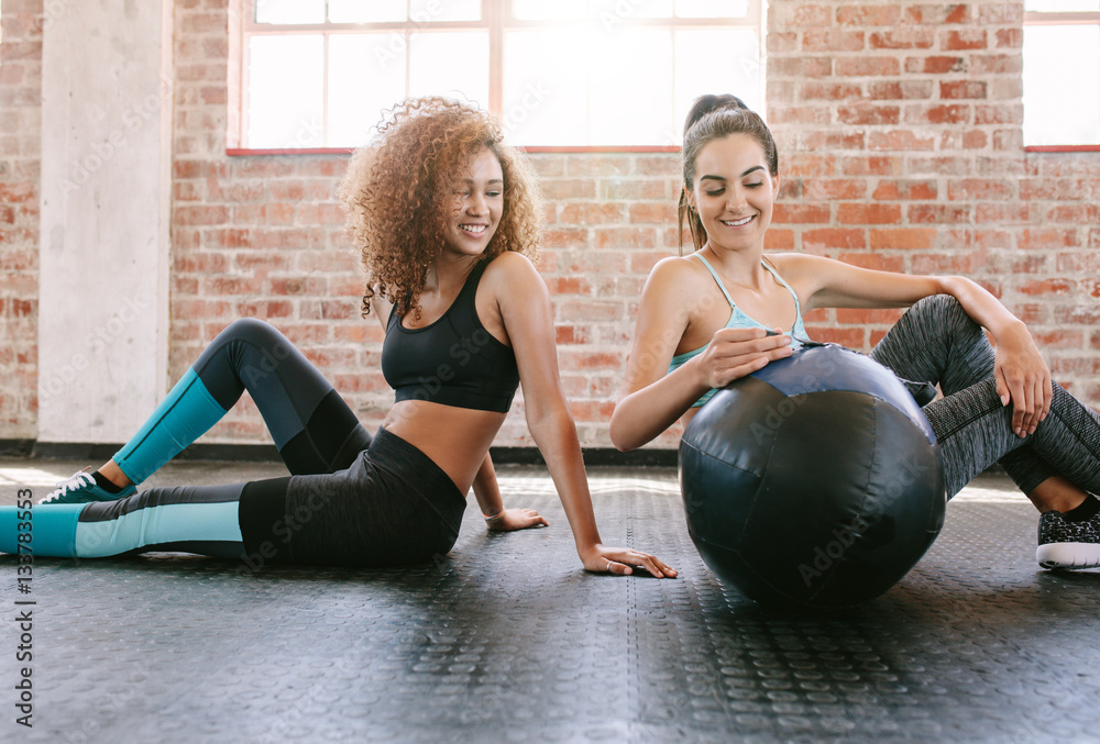 Two young female friends in gym with medicine ball