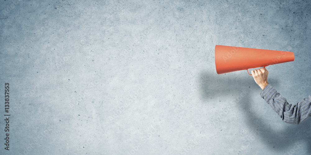 Hand of man holding paper trumpet against concrete background