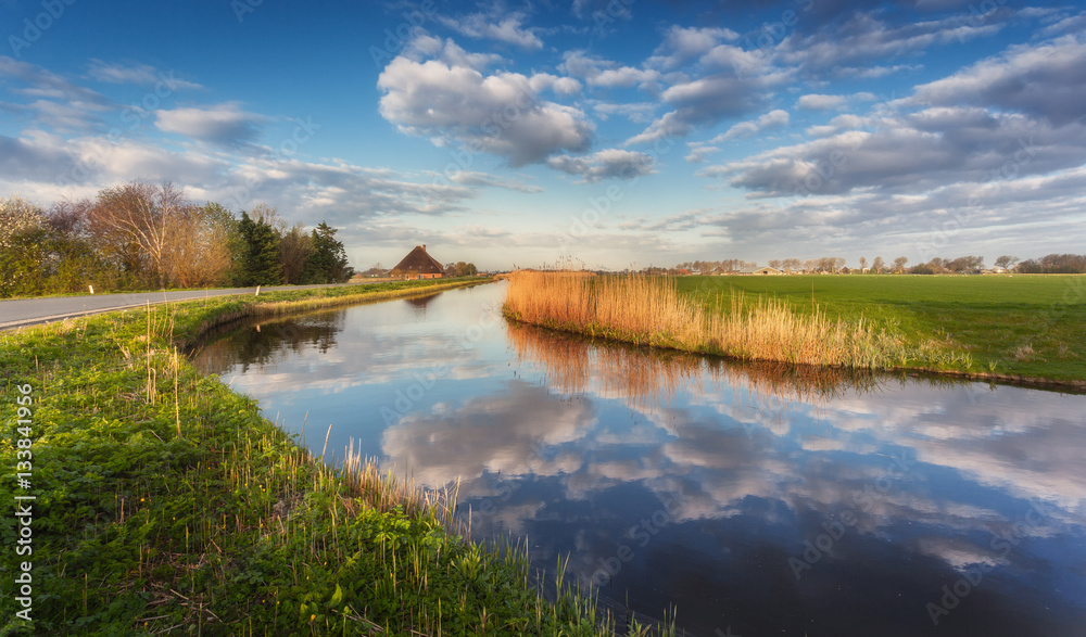 Buildings and trees near the water canal at sunrise in Netherlands. Colorful blue sky with clouds. S