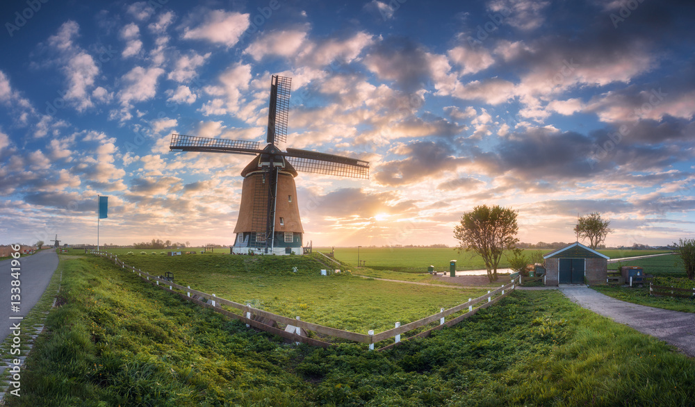 Windmill at sunrise in Netherlands. Beautiful old dutch windmill, green grass, fence  against colorf